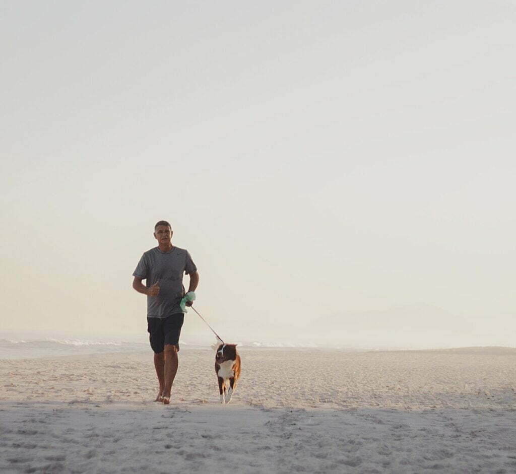 A man and his dog walking on the beach. It appears the man is leash training his dog.